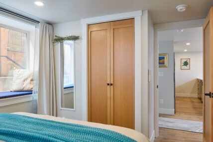Basement bedroom with partially below ground window on left and wooden closet door on right.