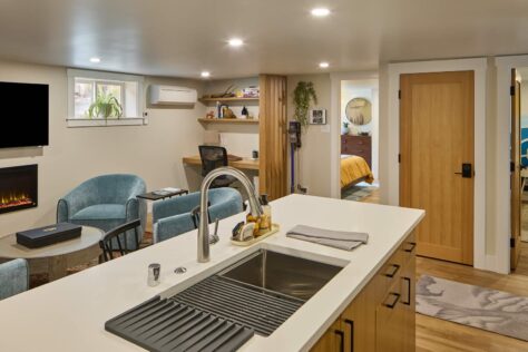 Basement kitchen sink with living room and fireplace in background.