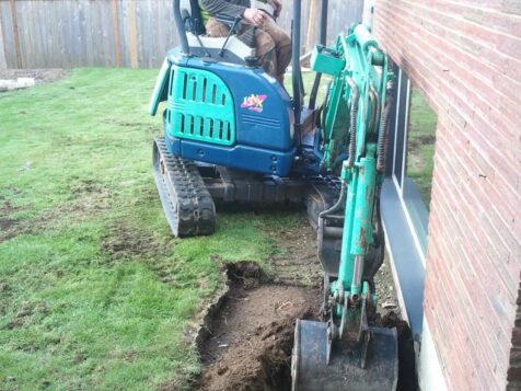 Man using a backhoe to expose house foundation